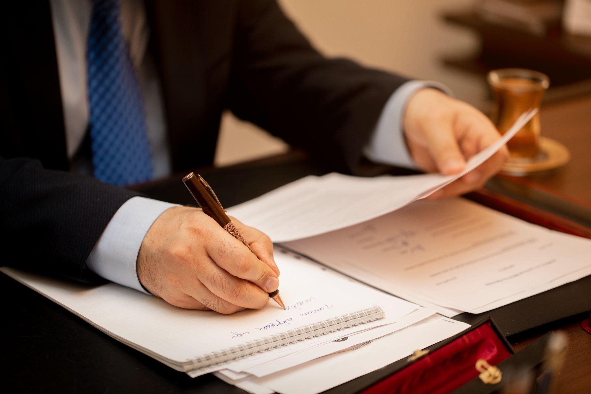 a person in a suit and tie is writing in the documents